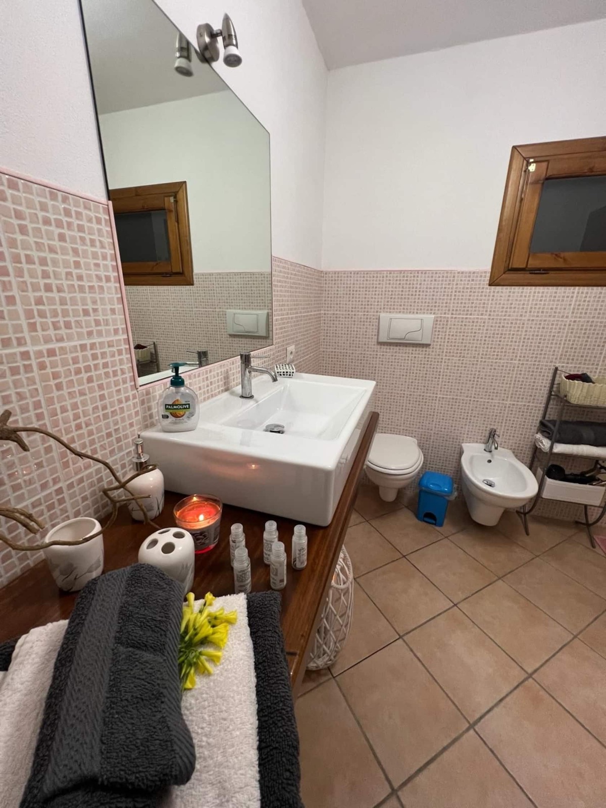 Bagno con mosaico rosa, lavabo su piano in legno e bidet